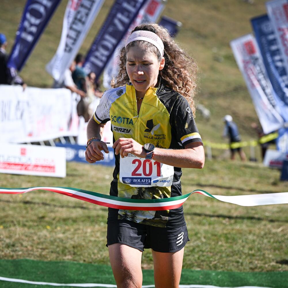 Atleti in corsa su percorso montano, tifosi in piedi, giornata di sole, gara di atletica